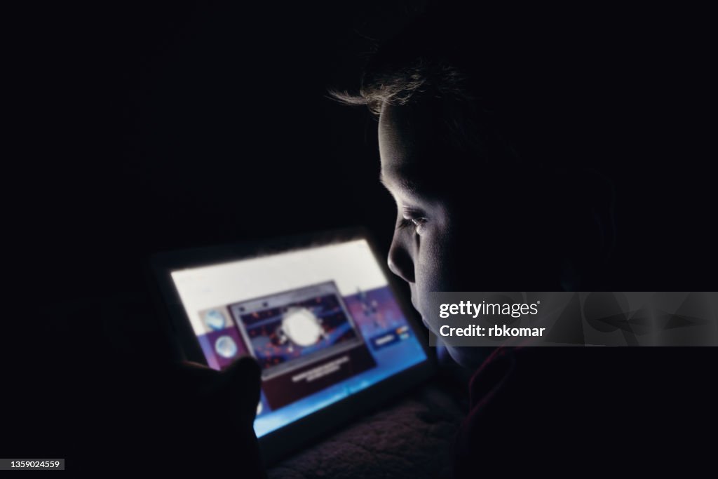 Little preschool boy holding digital mobile tablet lying on the sofa at night