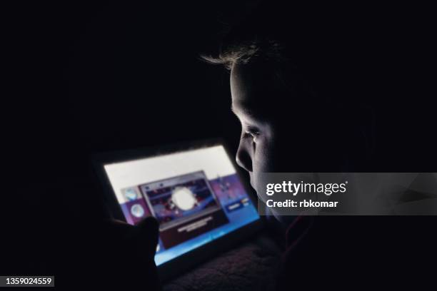 little preschool boy holding digital mobile tablet lying on the sofa at night - mobile game stock pictures, royalty-free photos & images