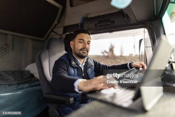 truck driver typing destination on tablet while sitting in cabin - veículo terrestre comercial imagens e fotografias de stock