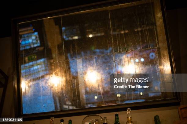 an antique mirror hangs in a restaurant with reflections of cool dusk and warm lights. - amsterdam dusk evening foto e immagini stock