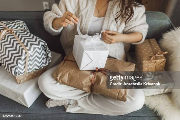 woman wrapping christmas presents near fir tree at cozy decorated home. - unboxing stock-fotos und bilder