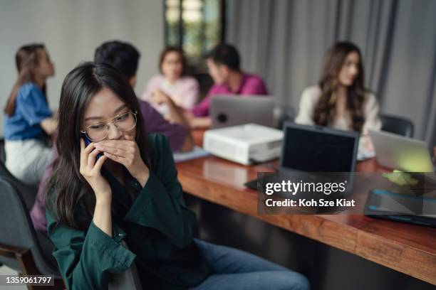 asian woman whispering on a phone call during a meeting - whispering stock pictures, royalty-free photos & images