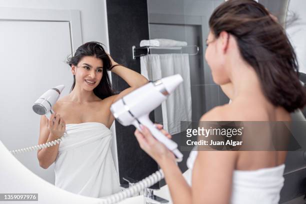 graceful hispanic lady using hair dryer near mirror in bathroom - blow drying hair stock pictures, royalty-free photos & images