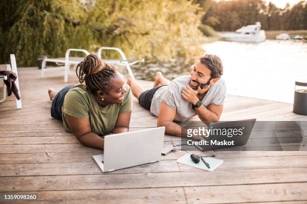 smiling female and male colleagues working on laptop at jetty by sea - time off work stock pictures, royalty-free photos & images