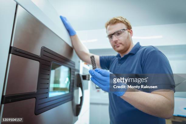 man holding metal 3d printed object in laboratory - blauer handschuh stock-fotos und bilder