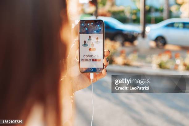 woman holding a phone in the street using the contact tracing app - contact tracing stock pictures, royalty-free photos & images