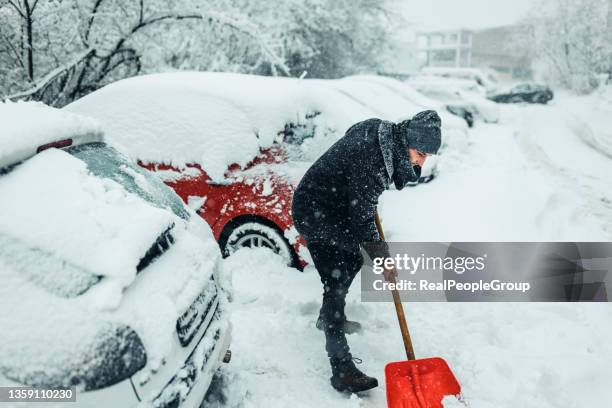 man with a snow shovel. car and street under snow. - snow shovel man stock pictures, royalty-free photos & images