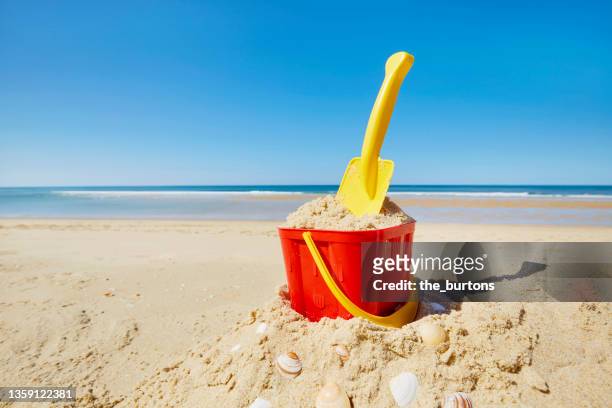 still life of bucket and shovel on sand castle at sea against blue sky - bucket and spade stock pictures, royalty-free photos & images