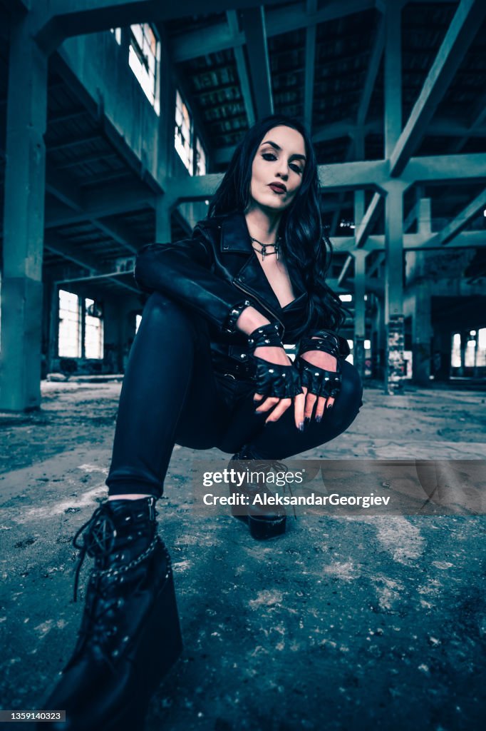 Beautiful Goth Female Dressed In Leather Kneeling In Abandoned Factory Ruins