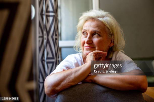 a senior woman leaning on the chair, looking through the window on her right side. - emotional intelligence stock pictures, royalty-free photos & images