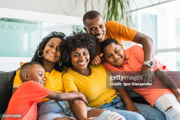 retrato de una familia feliz sentada en el sofá de la sala de estar - fond orange fotografías e imágenes de stock