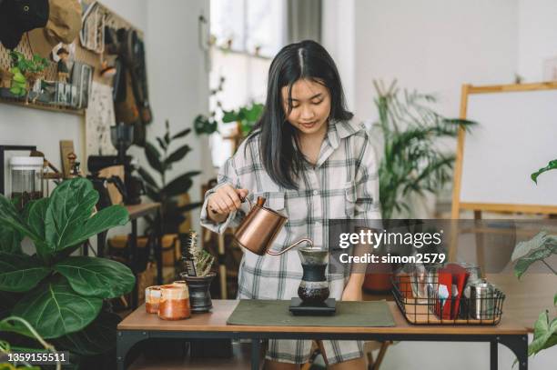 junge asiatin, die wasser auf kaffeemehl gießt und kaffee von hand tropft - filterkaffee stock-fotos und bilder