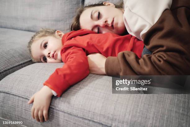 mother asleep on the couch over her daughter - fragilidad fotografías e imágenes de stock