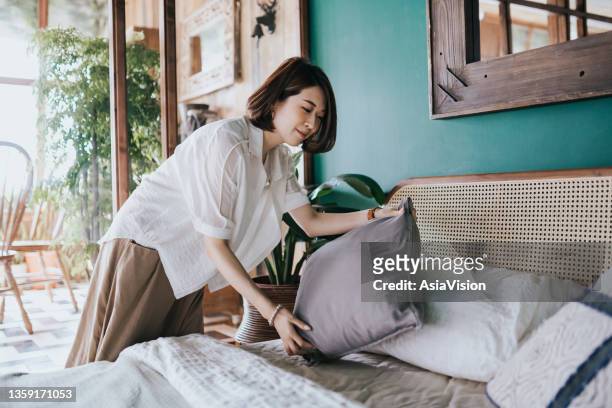young asian woman doing her morning routine, arranging pillows and making up her bed at home. let's get the day started - cushion imagens e fotografias de stock