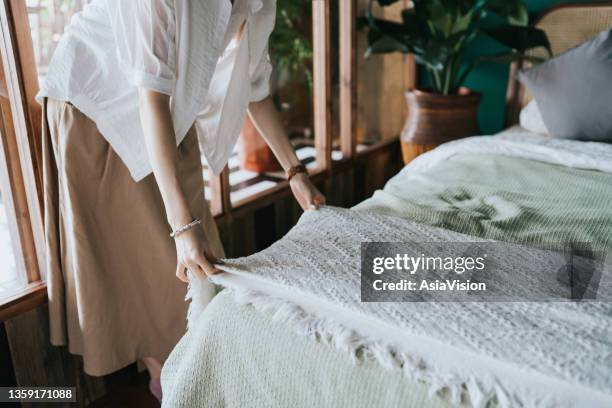 cropped shot of young asian woman doing her morning routine, making up her bed at home. let's get the day started - quilt imagens e fotografias de stock