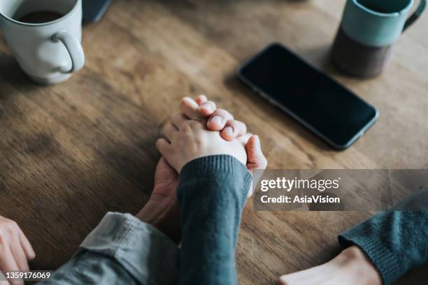 nahaufnahme eines jungen asiatischen paares bei einem date im café, händchen haltend am couchtisch. zwei tassen kaffee und ein smartphone auf holztisch. liebes- und pflegekonzept - hand resting on wood stock-fotos und bilder