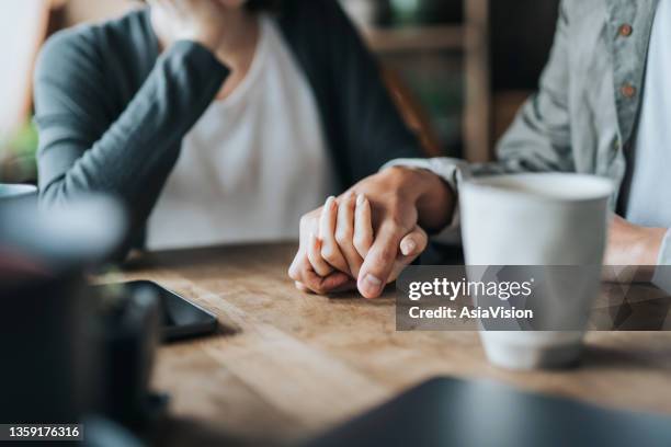 close up of young asian couple on a date in cafe, holding hands on coffee table. two cups of coffee and smartphone on wooden table. love and care concept - support stockfoto's en -beelden