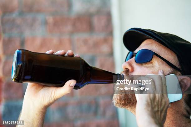 reifer mann trinkt bier aus der flasche, während er sein smartphone benutzt - beer bottle mouth stock-fotos und bilder