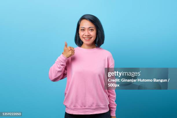 smiling asian woman showing thumbs up on blue background,indonesia - happy woman thumbs studio stock-fotos und bilder