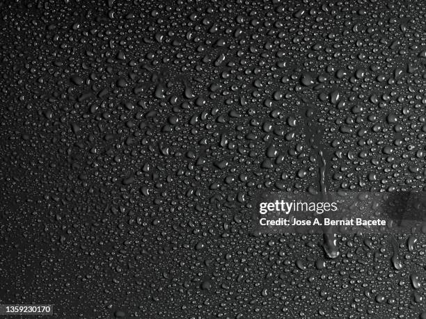 full frame of the water droplets sliding on a black wet surface. - dew stock pictures, royalty-free photos & images