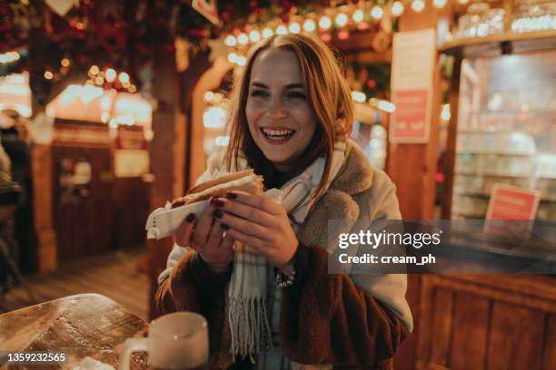 smiling woman enjoying a sausage at the christmas market - sausage roll stock pictures, royalty-free photos & images