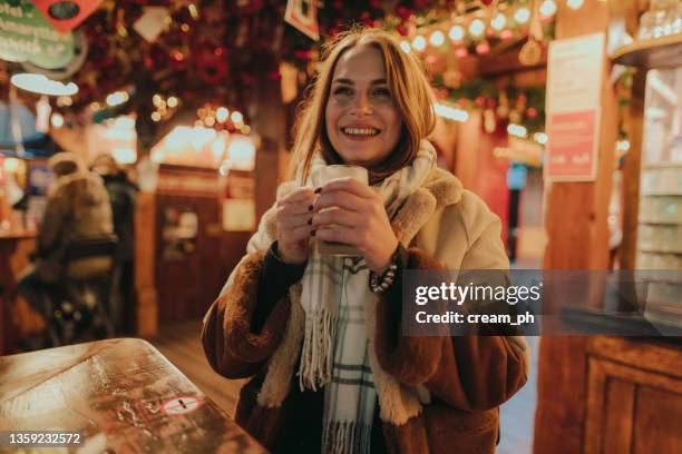 smiling woman enjoying a mulled wine at the christmas market - christmas market decoration stockfoto's en -beelden