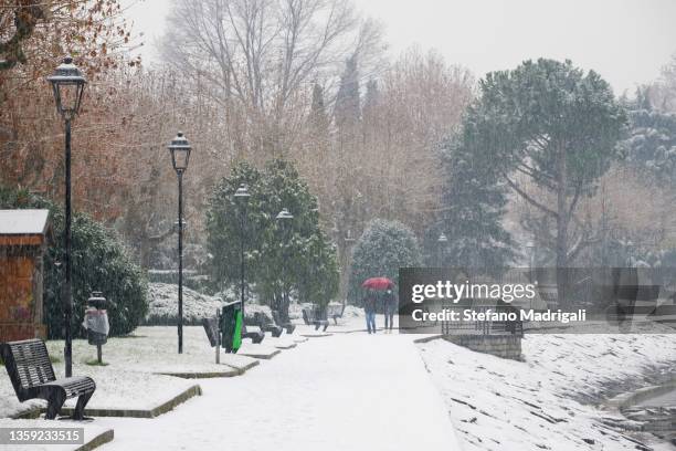 two people with umbrellas walk while it's snowing - schneeregen stock-fotos und bilder