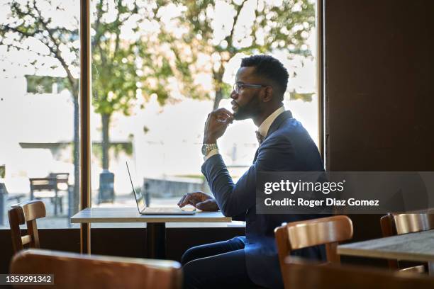 side view of an african-american man sitting in a coffee shop working on his laptop - internet cafe stock pictures, royalty-free photos & images