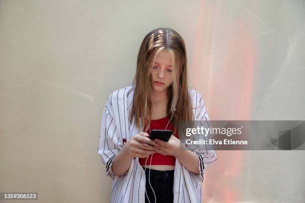 teenage girl using mobile phone and leaning against a white painted wall, with red reflections bounced off from the (out-of-frame) rear lights of a nearby vehicle, projected onto the wall - one teenage girl only bildbanksfoton och bilder