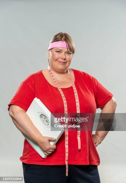post christmas dieting. proud overweight woman holding weight scale - voluptueus stockfoto's en -beelden