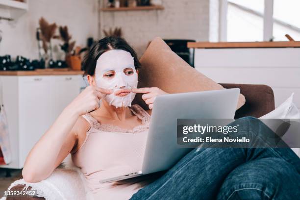 facial massage.  woman in a moisturizing mask massaging her face. a woman sits in a cozy chair and watches  online course on facial skin care. face fitness - skin care 個照片及圖片檔