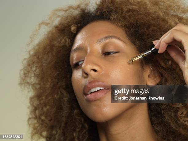 young woman applying beauty oil to face - apothecary bottle stock pictures, royalty-free photos & images