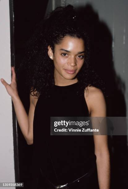 American actress Lisa Bonet , wearing a black sleeveless top, her right hand resting on a doorframe, May 1986.