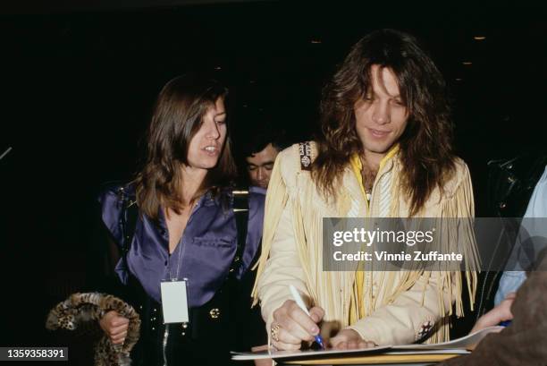 American singer, songwriter and guitarist Jon Bon Jovi, wearing a tan fringed leather jacket over a yellow shirt, signing programmes for fans...