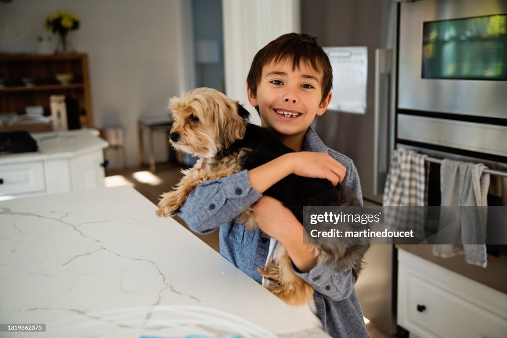 Young boy holding morki dog in kitchen.