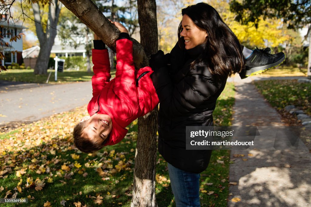 Mother helping son to get down a tree branch in autumn.