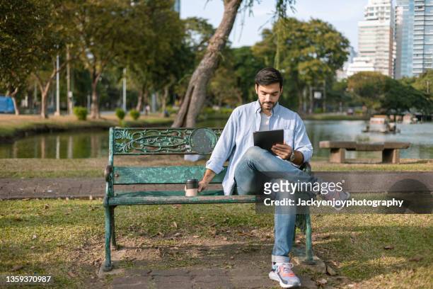 businessman using digital tablet,sitting on bench in the lumpini park,bangkok ,thailand - parkbank stock-fotos und bilder