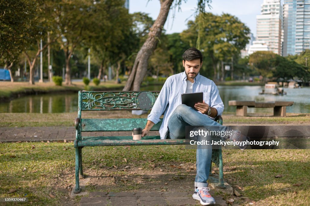 Businessman using digital tablet,Sitting on bench in the Lumpini park,bangkok ,Thailand