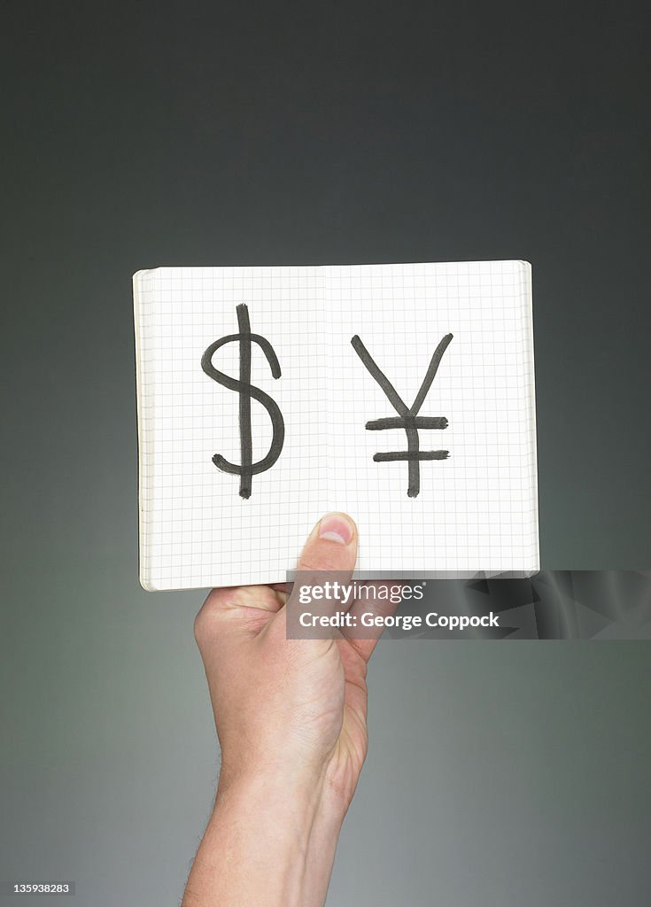 Hand holding Us Dollar and Chinese Yen in notebook
