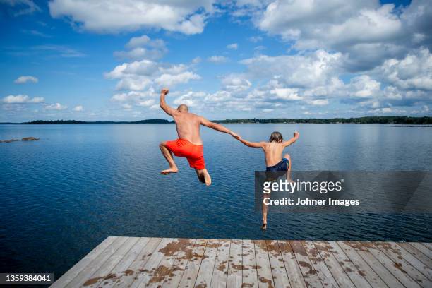 father and son jumping into sea - bathing jetty stock pictures, royalty-free photos & images