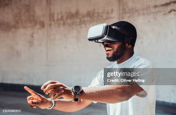 young african american man uses virtual reality glasses and has fun with it - cyberspace stockfoto's en -beelden