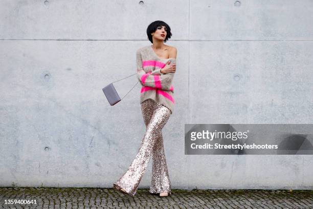 Model Zoe Helali wearing a beige and pink striped knitted pullover by Miss Goodlife, champagne colored flared sequin pants by Miss Goodlife, nude...