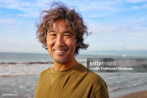 portrait of genuine surfer man in 50s with smile - asian on beach bildbanksfoton och bilder
