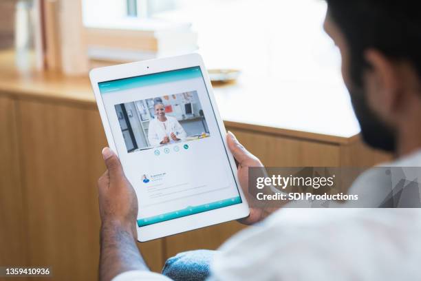 over the shoulder view man using telehealth app on tablet - male influencer stock pictures, royalty-free photos & images