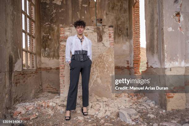 androgynous guy with curly hair, vintage clothes and high heels looking at camera in an abandoned factory - artists model stock-fotos und bilder