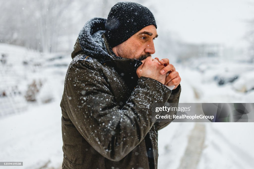 Portrait shot of the caucasian good looking mature man in casual style is freezing on the cold winter day while standing in the center city.
