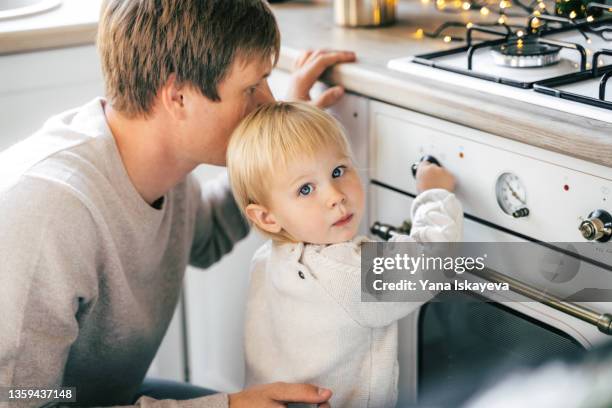 bright portrait of a cute baby toddler and father cooking at home kitchen, looking at camera - burner stove top stockfoto's en -beelden