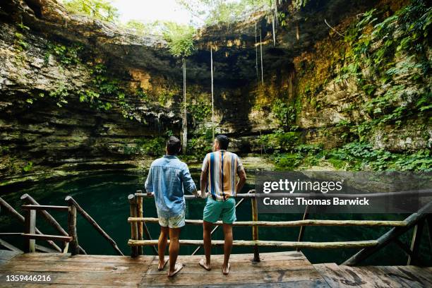 wide shot rear view of gay couple looking around cenote before going swimming - groen shirt stockfoto's en -beelden