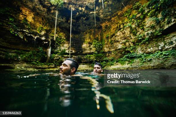 Wide shot view from water of gay couple swimming together in cenote