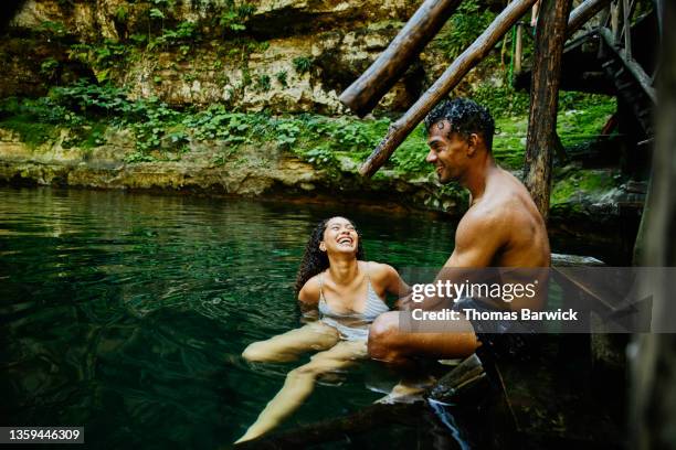 wide shot of laughing couple hanging out on stairs into cenote after swimming - adventure travel stock pictures, royalty-free photos & images